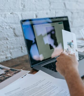 pexels-photo-7128957-7128957-1 A person reviews photographs on a desk with a laptop, in a modern workspace.