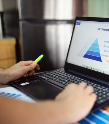 pexels-photo-7948005-7948005 Person analyzes business data on laptop, using pyramid chart and financial reports.